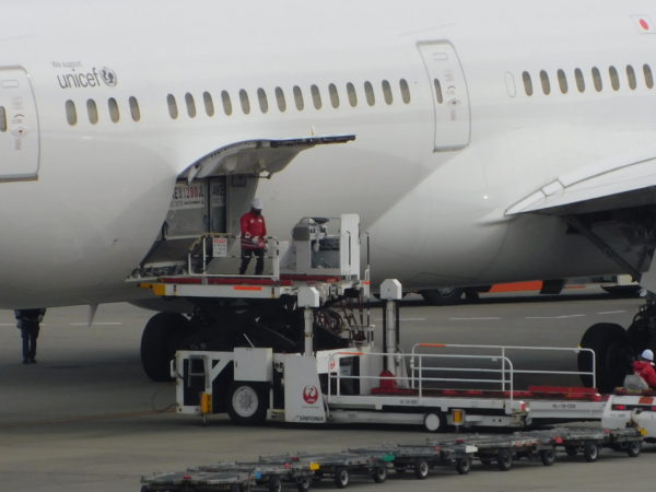 機体に搭載されたコンテナをドーリーに移すための準備作業の写真